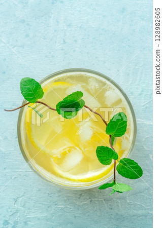 A glass of fresh lemonade, a mocktail with lemon juice, on a blue background A glass of fresh lemonade, a mocktail with lemon juice, on a blue background 128982605