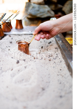 Preparing traditional Turkish coffee in sand with copper pot and hand 128982680