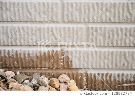 Painting block exterior wall with dirt stains and loose gravel near the foundation of a house 128982754