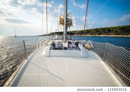 Sailing yacht anchored near uninhabited islands in Croatia, captured from the bow. Peaceful summer stopover and maritime leisure in a remote coastal area. 128983016