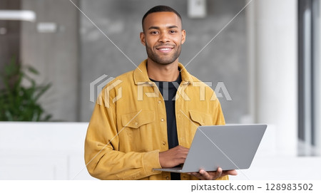 Smiling man using a laptop in a modern workspace. 128983502