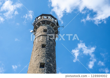The Svatobor lookout tower stands tall with its rugged stone exterior, surrounded by bright blue skies and fluffy clouds. Visitors can enjoy panoramic views from its height. The Svatobor lookout tower stands tall with its rugged stone exterior, surrounded by bright blue skies and fluffy clouds. Visitors can enjoy panoramic views from its height. 128984002