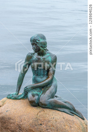 The iconic Little Mermaid statue sits gracefully on a rock in Copenhagen, Denmark. Surrounded by tranquil waters, it offers a serene view for visitors. 128984026