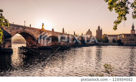 Morning sunlight casts a warm glow over the Vltava River as the iconic Charles Bridge stands majestically, reflecting the beauty of Prague's historic architecture along the embankment. Morning sunlight casts a warm glow over the Vltava River as the iconic Charles Bridge stands majestically, reflecting the beauty of Prague's historic architecture along the embankment. 128984082