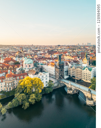 Overlooking the Vltava River, Charles Bridge connects the historic districts of Prague. The Old Town Bridge Tower stands majestically, surrounded by the vibrant skyline and lush trees. Overlooking the Vltava River, Charles Bridge connects the historic districts of Prague. The Old Town Bridge Tower stands majestically, surrounded by the vibrant skyline and lush trees. 128984095