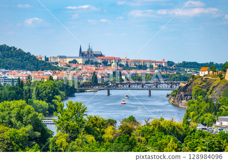 Panoramic overlook from Podoli showcases the Vltava River winding through Prague. Historic buildings, lush greenery, and boats on the river contribute to the city's charm. Panoramic overlook from Podoli showcases the Vltava River winding through Prague. Historic buildings, lush greenery, and boats on the river contribute to the city's charm. 128984096