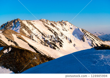 Mount Oyama and Mount Onamichi of the Tateyama mountain range dyed in the sunset (view from Tsurugi-Gozenmae) Climbing Mount Tateyama and Mount Betsuyama in the Northern Alps with remaining snow 128985994