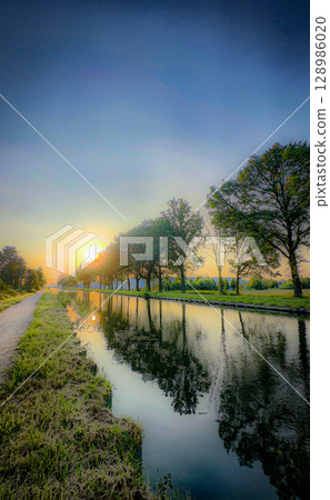 Serene Sunrise Reflections Along a Beautiful and Tranquil Canal Pathway in Natures Splendor Serene Sunrise Reflections Along a Beautiful and Tranquil Canal Pathway in Natures Splendor 128986020