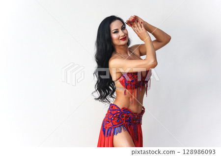 Brunette in Red Dress Performing Eastern Dance Movements Against a White Background 128986093