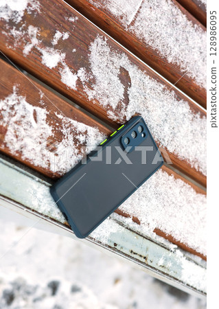 Forgotten mobile phone on a wooden bench: negligence and inattention of people 128986095