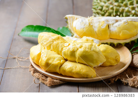 Ripe durian fruit or Durio zibethinus with yellow creamy pulp exposed on wood plate Ripe durian fruit or Durio zibethinus with yellow creamy pulp exposed on wood plate 128986383