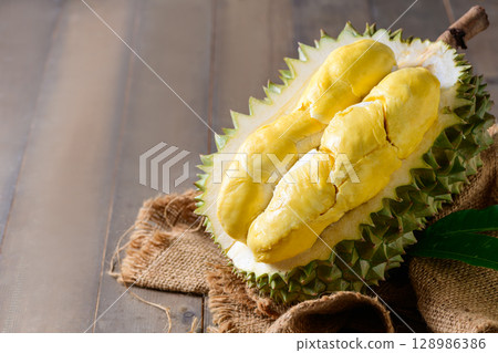 Ripe durian fruit or Durio zibethinus with yellow creamy pulp exposed, isolated on white background. 128986386