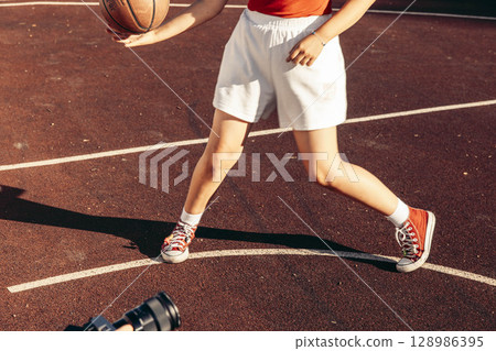 teen legs in motion while playing basketball on outdoor court, wearing red sneakers and white sports shorts, concept of movement, sport product, young athlete training 128986395