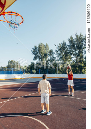 playground basketball practice with boy and girl in casual clothes, large open court with copy space, concept of teen wellness, afterschool sport program 128986400