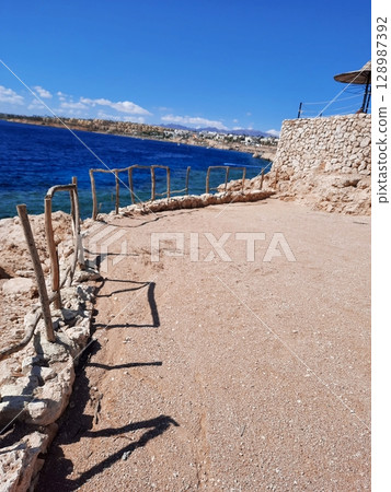 Coastal Pathway with Stone Wall and Wooden Fence Overlooking Deep Blue Ocean Coastal Pathway with Stone Wall and Wooden Fence Overlooking Deep Blue Ocean 128987392