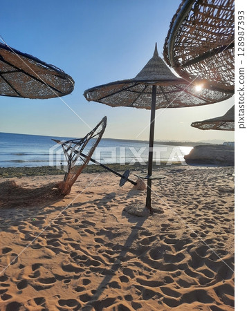 Sandy Beach with Woven Parasols and Calm Blue Ocean at Sunset Sandy Beach with Woven Parasols and Calm Blue Ocean at Sunset 128987393