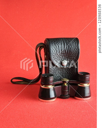 Vintage black theatre binoculars with a black leather case on red background. Made in USSR. 1960s. 128988536