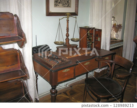 A classic wooden desk with an abacus, a balance scale, and a small cabinet, set against a framed picture in a historical office space A classic wooden desk with an abacus, a balance scale, and a small cabinet, set against a framed picture in a historical office space 128989213