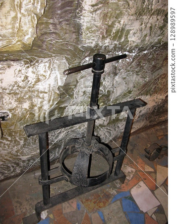 A black iron head press with a screw mechanism, set against a rugged stone wall in a dimly lit historical torture chamber 128989597