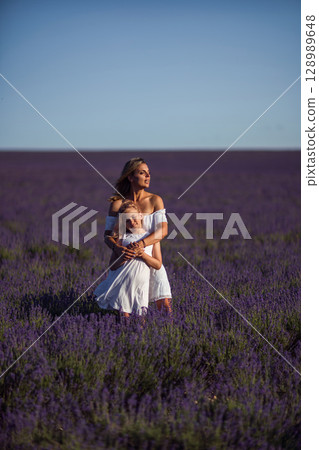 Lavender Mother Daughter: Hugging in white dresses in vast purple field on sunny summer day, bonding. 128989648