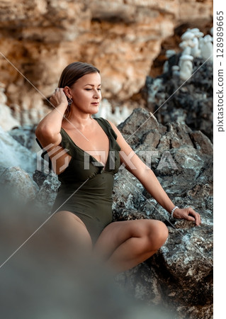 Woman Beach Rocks Green Swimsuit, a woman wearing a green swimsuit sits on a rock on a beach. 128989665