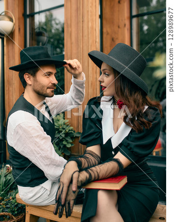 Woman in black dress with gloves leaning forward while man lifts hat in greeting 128989677