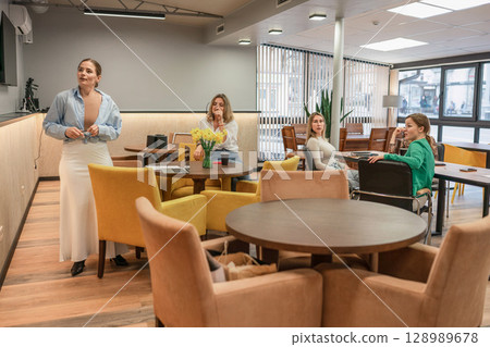 Meeting Women Discussion: Daytime office meeting features four women discussing business in a modern lounge area. 128989678