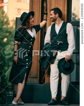 Woman in vintage dress smiling at man leaning on doorway 128989690