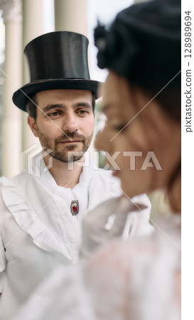 Man in top hat gazing at woman in blurred foreground in vintage setting 128989694