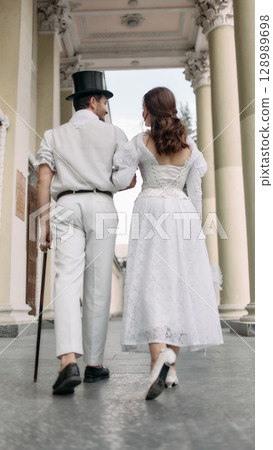Couple in vintage clothing walking away arm in arm near historic columns Couple in vintage clothing walking away arm in arm near historic columns 128989698