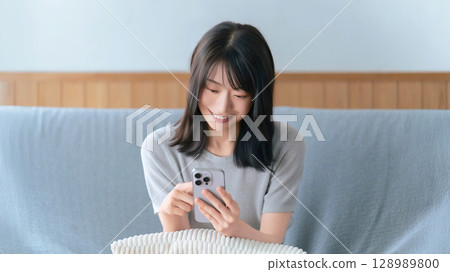 微笑的女人坐在沙發上使用智慧型手機 微笑的女人坐在沙發上使用智慧型手機 128989800