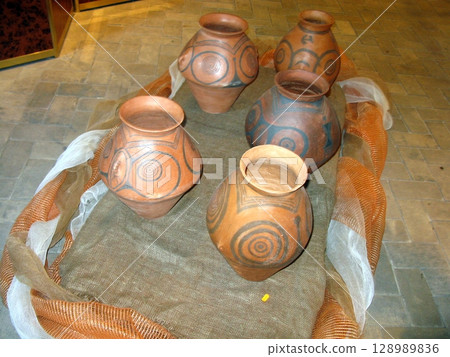 A collection of intricately patterned terracotta vases displayed on a burlap mat with orange and white fabric accents on a tiled floor 128989836