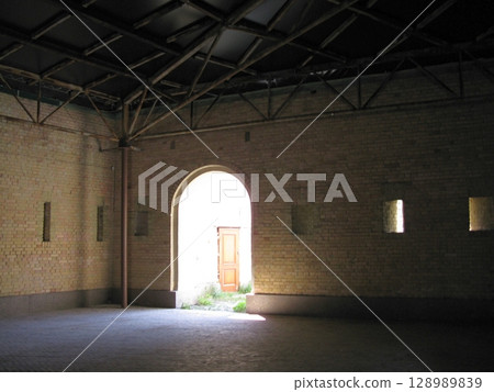 A dimly lit brick hall with an arched doorway and a wooden door, illuminated by natural light, showcasing a historical architectural space 128989839