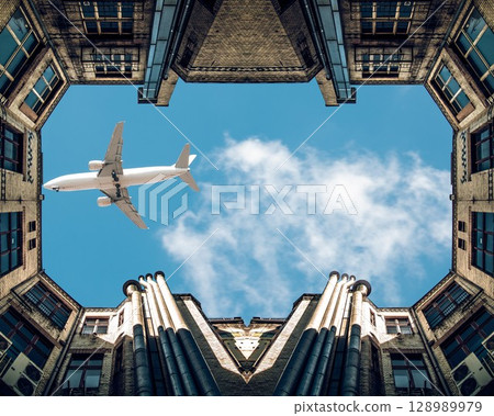 A large passenger plane flies low over city buildings, visible against the blue sky. A large passenger plane flies low over city buildings, visible against the blue sky. 128989979