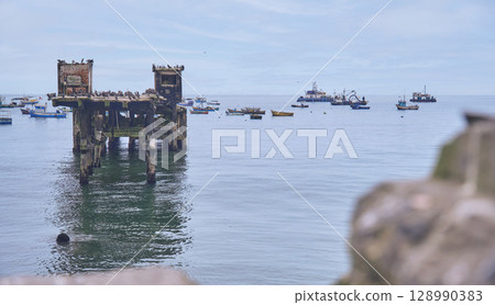 A large pier is visible in the water with many boats in the background, Chancay Lima, Peru. A large pier is visible in the water with many boats in the background, Chancay Lima, Peru. 128990383