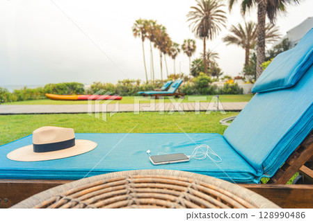 A blue lounge chair with a straw hat on it and a cell phone on it 128990486