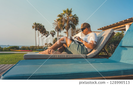 A man is sitting on a lounge chair with a laptop on his laptop. remote work concept A man is sitting on a lounge chair with a laptop on his laptop. remote work concept 128990513