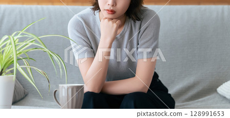 Woman sitting on the sofa in the living room thinking 128991653