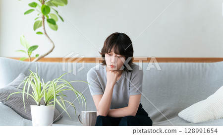 Woman sitting on the sofa in the living room thinking 128991654