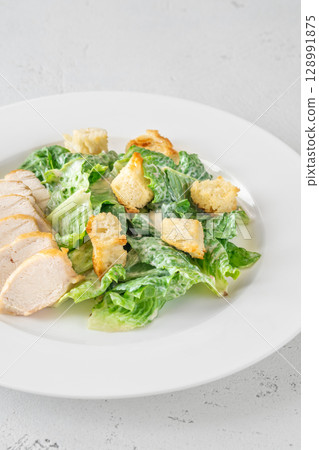 Classic Caesar salad topped with chicken breast served on clean white plate 128991875