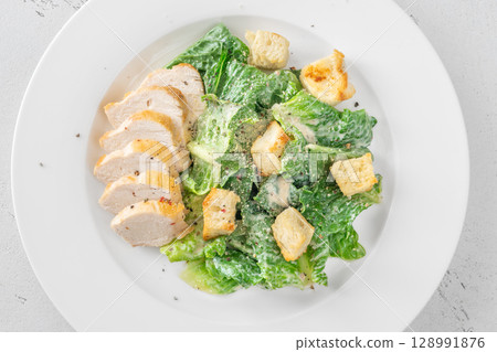 Classic Caesar salad topped with chicken breast served on clean white plate Classic Caesar salad topped with chicken breast served on clean white plate 128991876