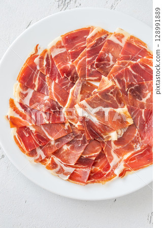 Thin Slices of Jamon Iberico Arranged on White Round Plate for Serving 128991889