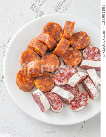 Assorted Spanish Chorizo and Fuet Sausage Slices on Minimal White Background Assorted Spanish Chorizo and Fuet Sausage Slices on Minimal White Background 128991893