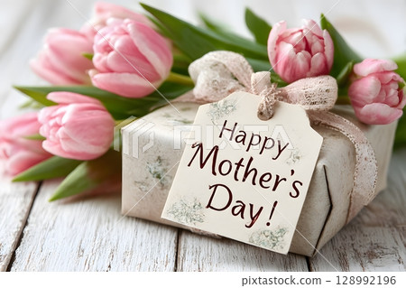 This festive scene features a thoughtful gift package for Mother's Day, elegantly presented alongside vibrant pink tulip flowers on a textured wooden surface. 128992196