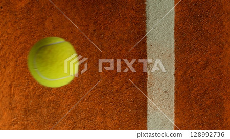 Freeze Motion Detail Shot of Tennis Ball Hitting a Clay Court 128992736