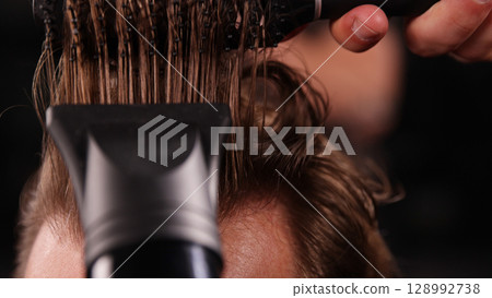 Young Man with Beard at Barber Shop. Barber is Preparing his Haircut. Dark Atmosphere, Black Background. Concept of Barber and a Client. Young Man with Beard at Barber Shop. Barber is Preparing his Haircut. Dark Atmosphere, Black Background. Concept of Barber and a Client. 128992738