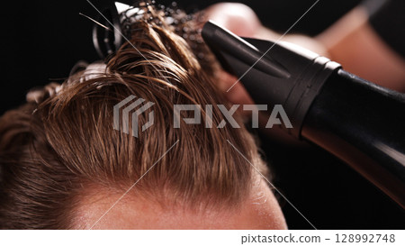 Young Man with Beard at Barber Shop. Barber is Preparing his Haircut. Dark Atmosphere, Black Background. Concept of Barber and a Client. 128992748