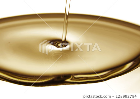 Pouring oil in golden tones. The texture of a cosmetic or other oil product. 128992784