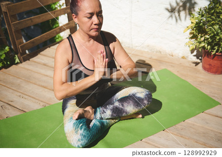 Woman Practicing Outdoor Yoga Meditation on Wooden Deck 128992929