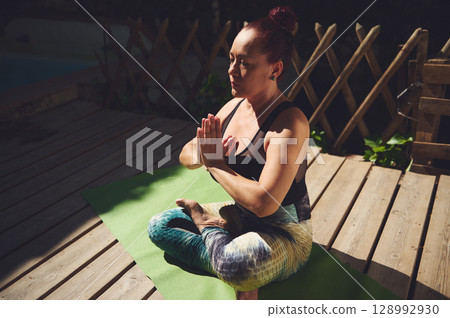 Woman Practicing Yoga Outdoors on a Wooden Deck on a Sunny Day 128992930